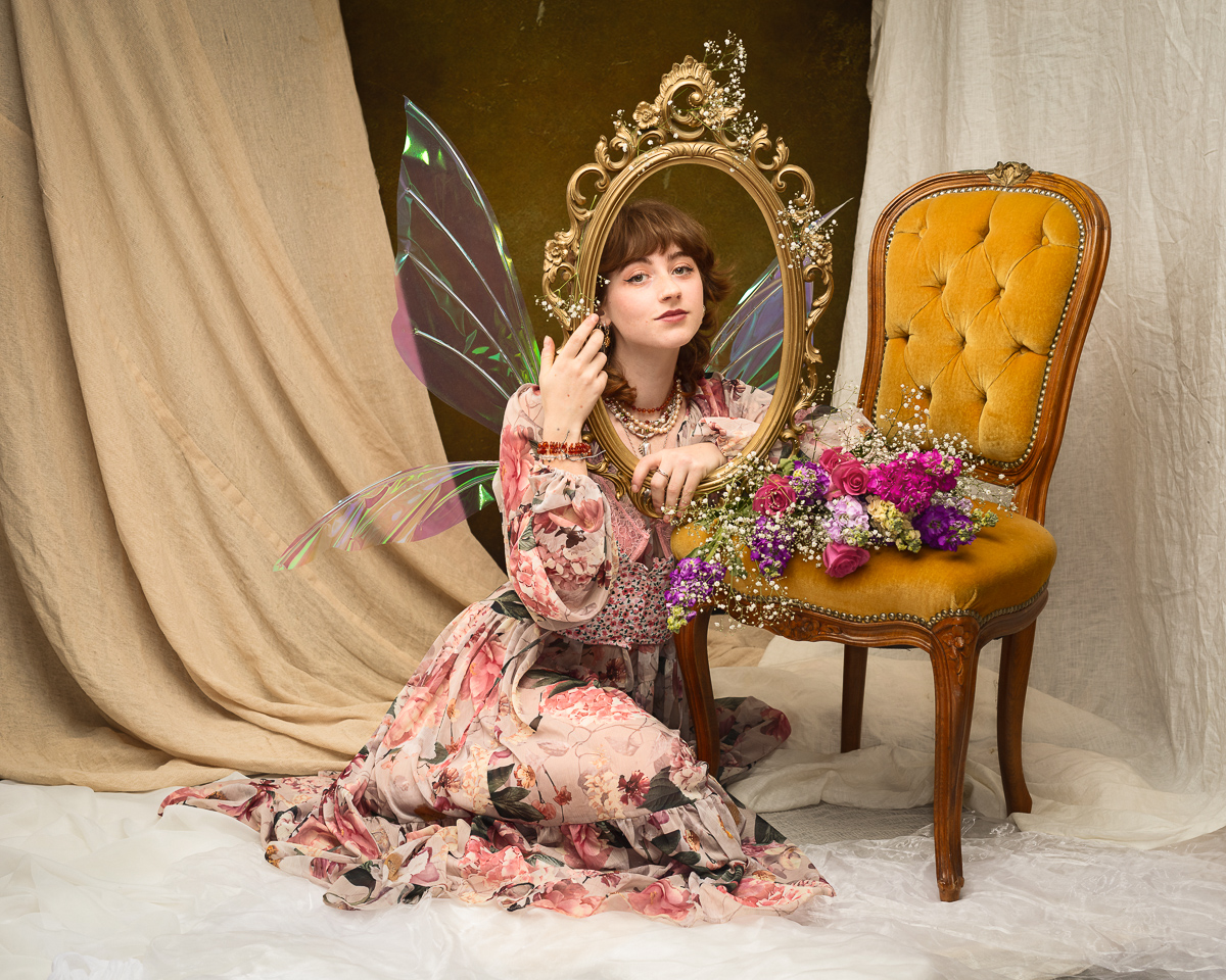 Woman with wings holding ornate mirror and flowers.