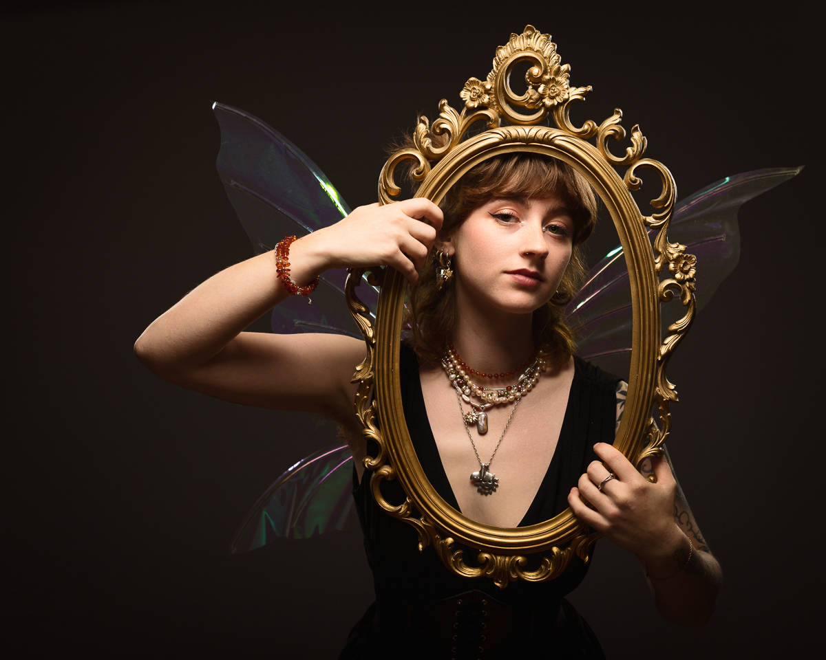 Person with fairy wings holding ornate frame.