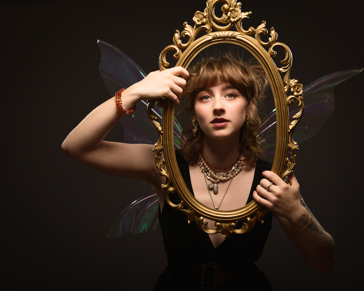 Woman in wings holds ornate mirror frame