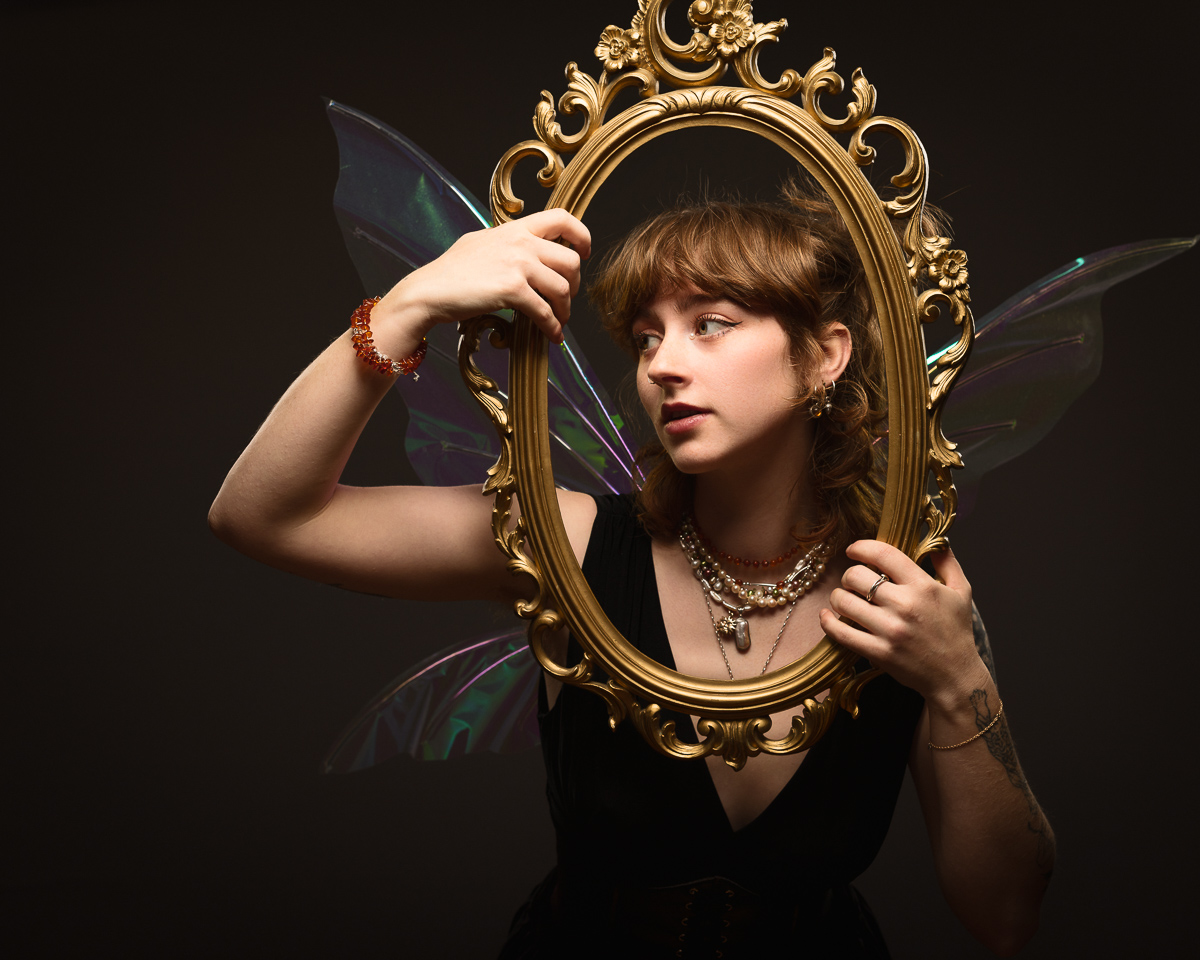 Woman with fairy wings holding ornate frame.