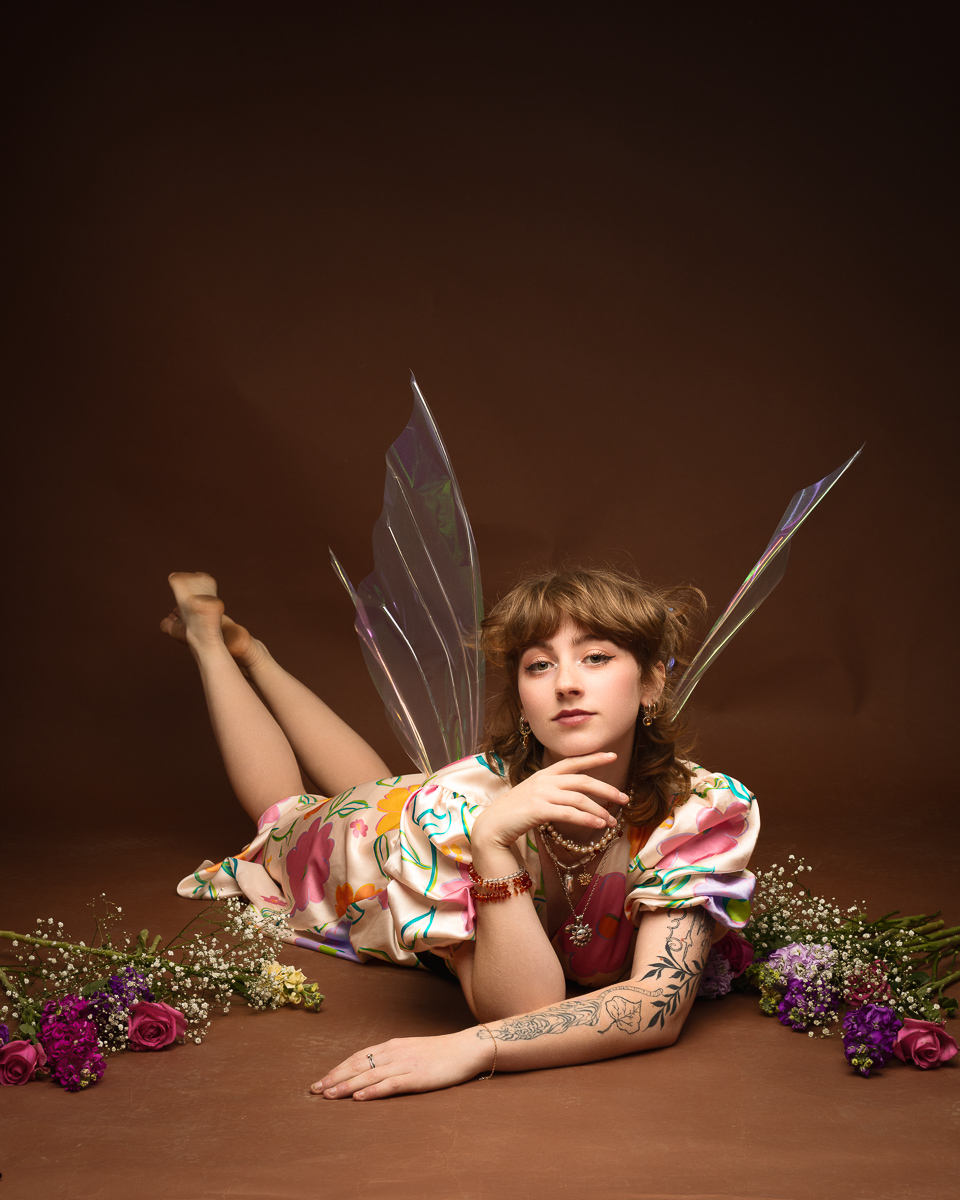 Woman in floral outfit with fairy wings and flowers.