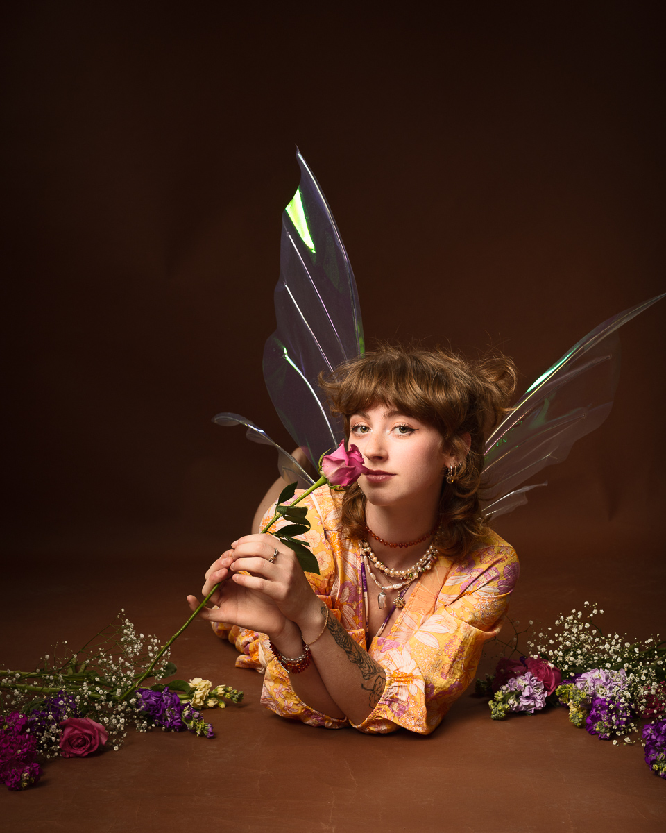 Person with wings surrounded by flowers, holding rose.