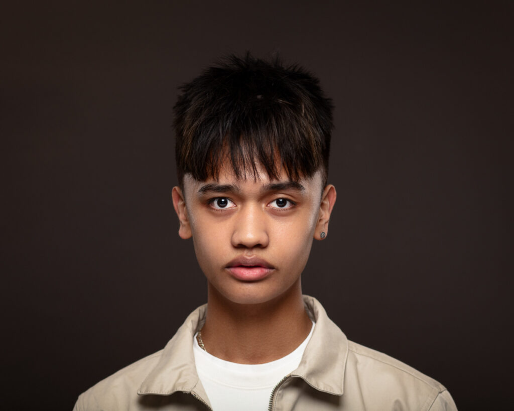 Young person with short hair, neutral expression, dark background.