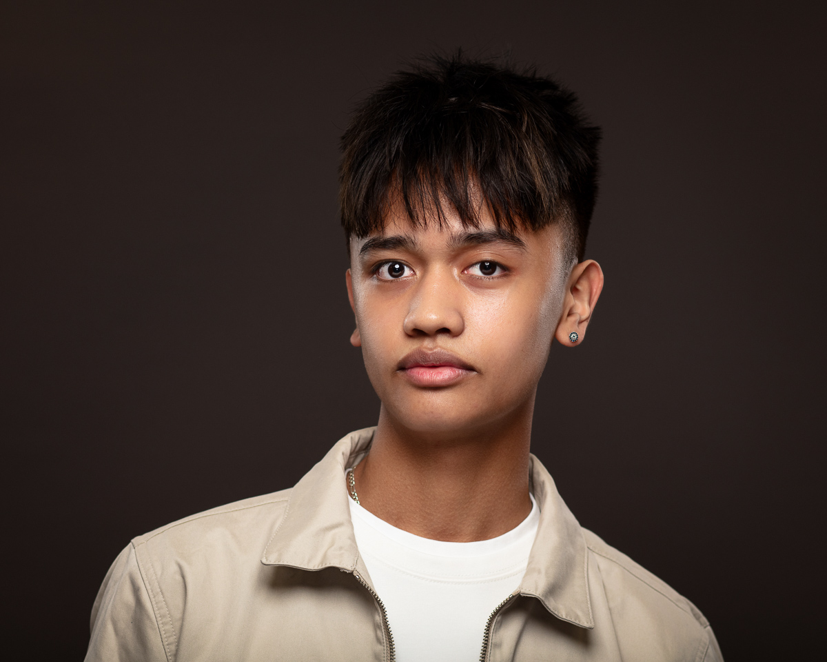 Young person in beige jacket, serious expression.