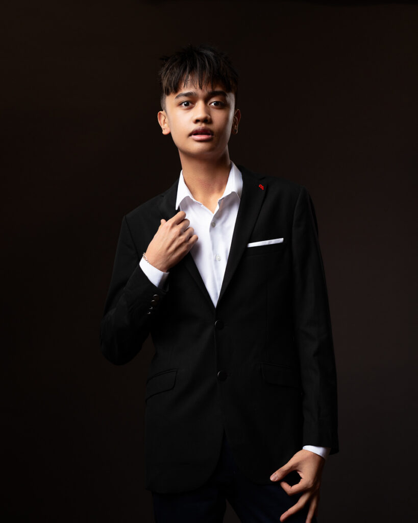 Young man in black suit, dramatic lighting.