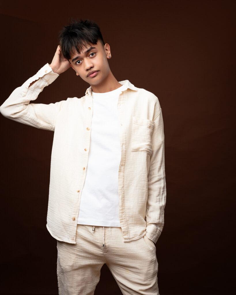 Person in cream outfit posing against brown background.