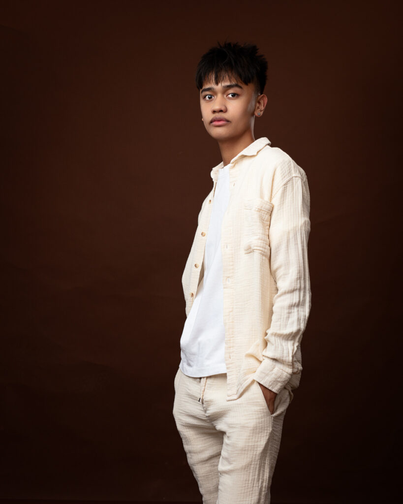 Person in cream outfit against brown background.