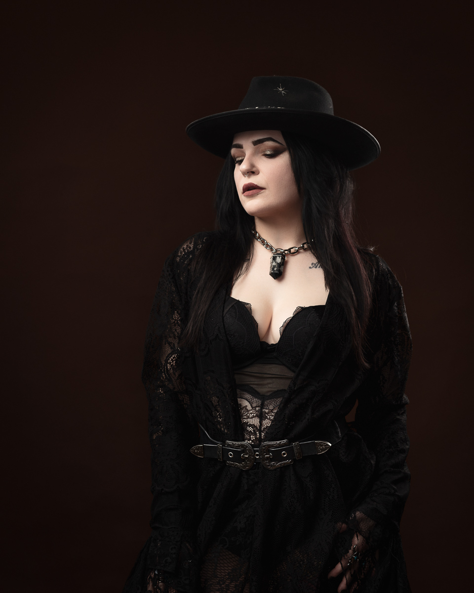 Woman in gothic attire with wide-brimmed hat.