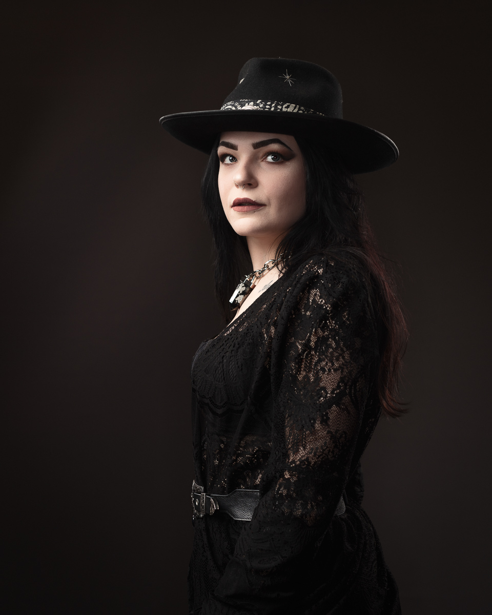 Person in black outfit wearing a hat, serious expression.
