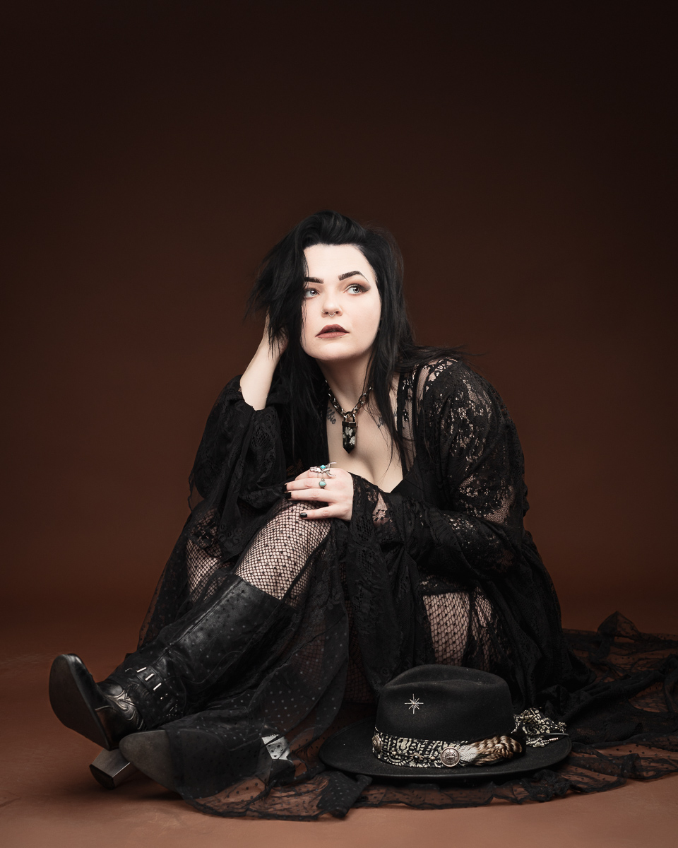 Woman in black gothic attire, seated on floor.