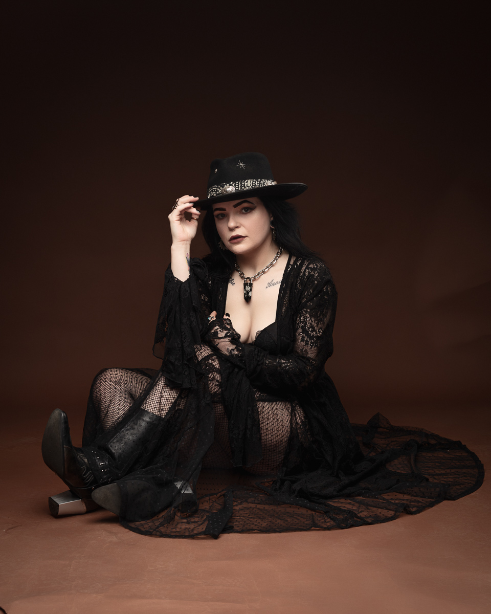 Person in black gothic attire with hat, dark background