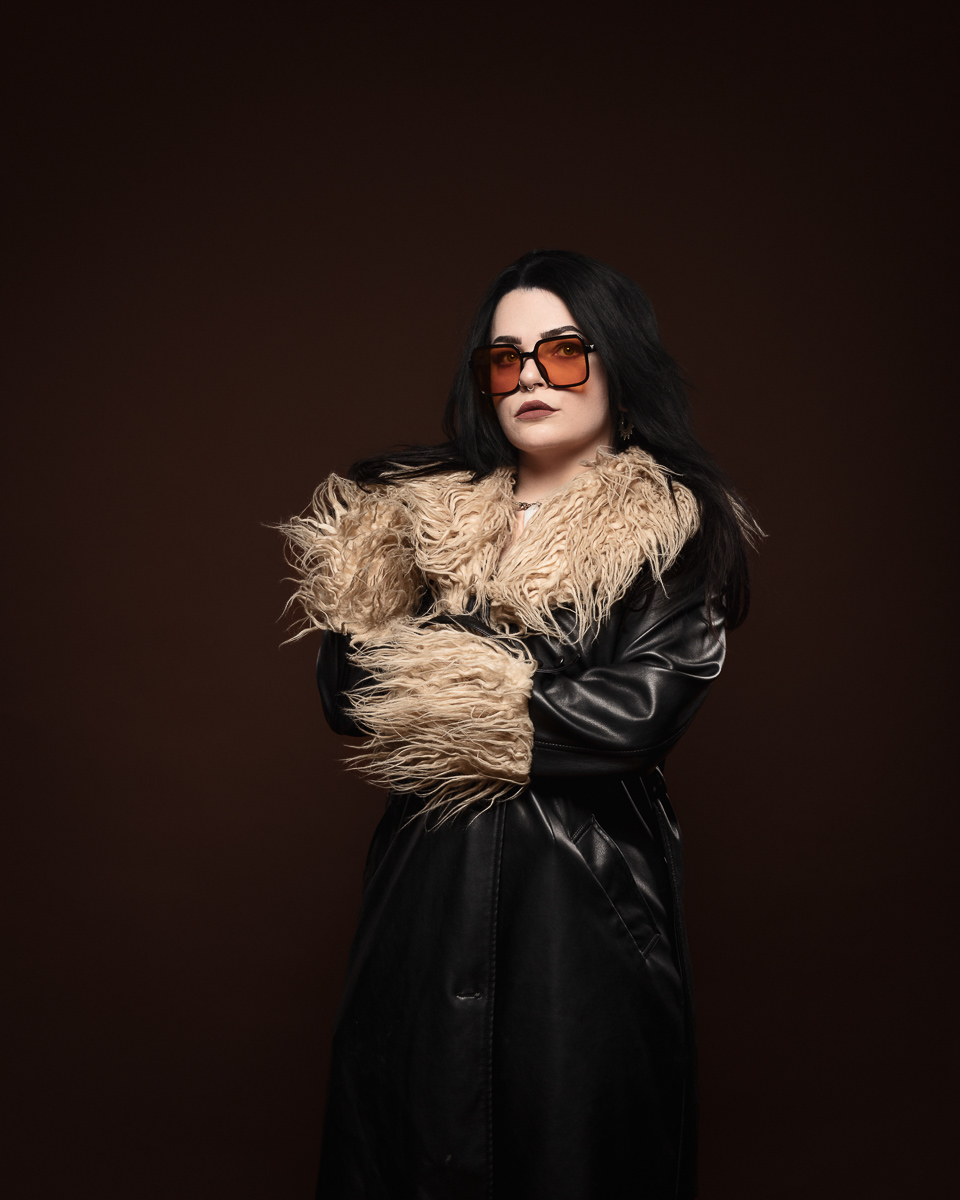 Person in vintage coat and sunglasses, serious expression.