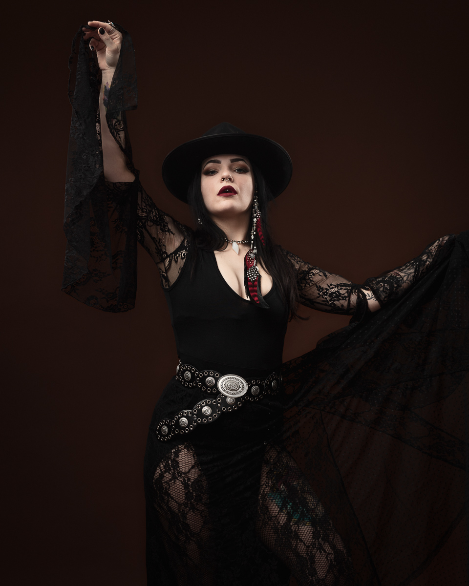 Woman in lace dress and wide-brimmed hat posing.