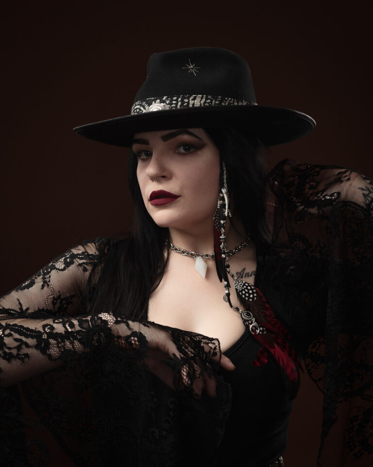 Person in black hat and lace clothing poses stylishly.