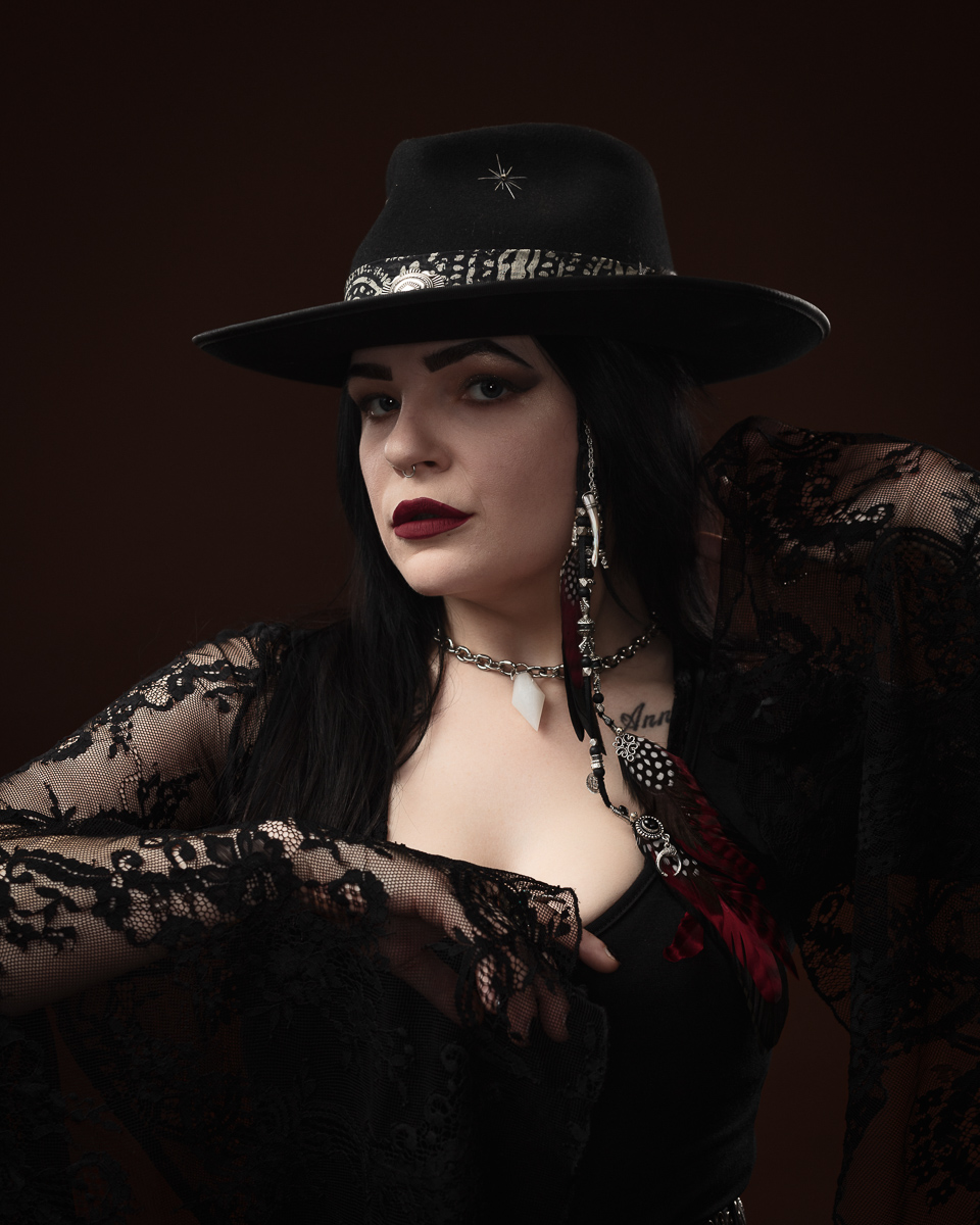 Person in black hat and lace clothing poses stylishly.