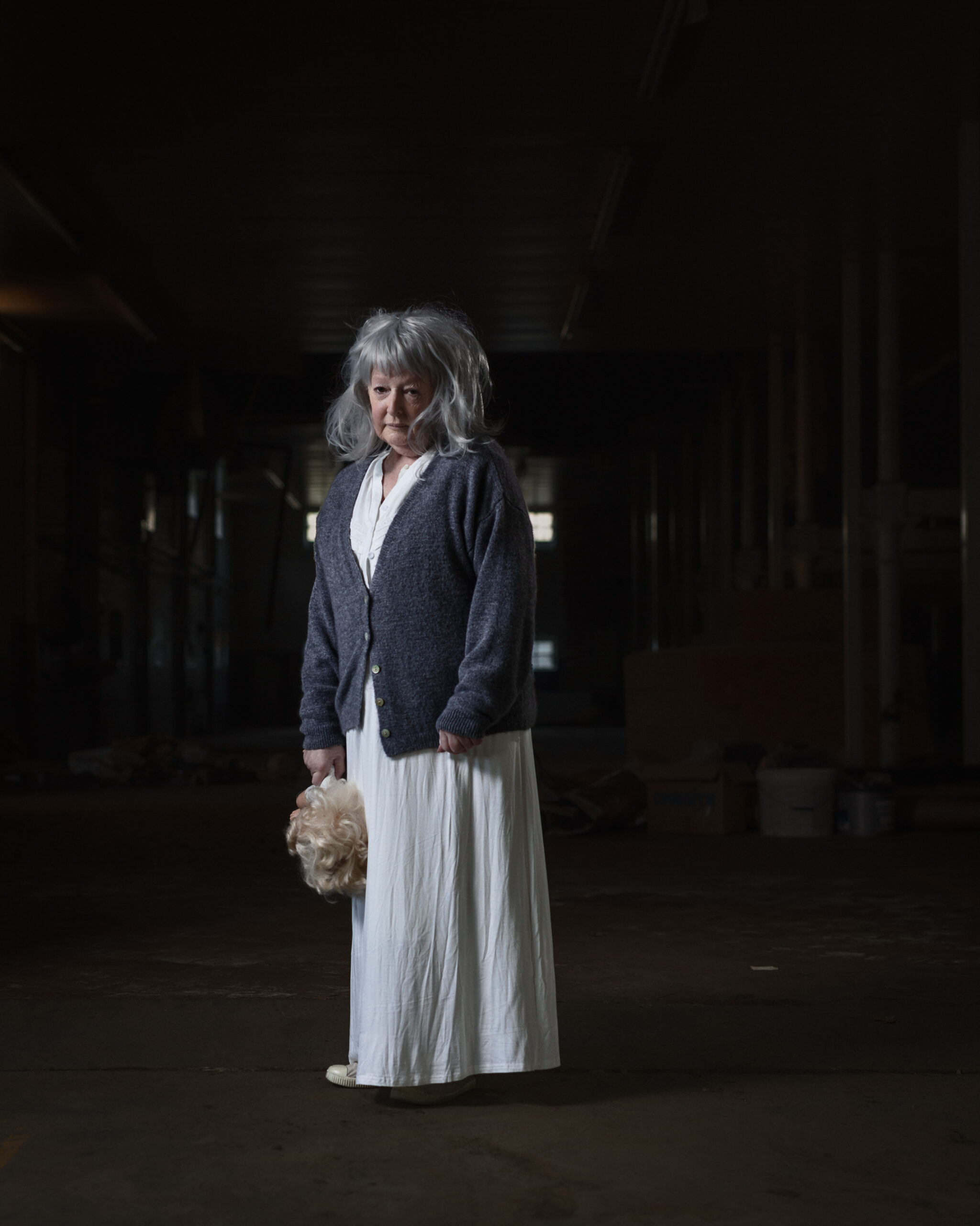 Elderly woman holding doll's head in dark room.