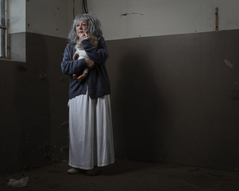 Elderly woman with doll in dimly lit room.