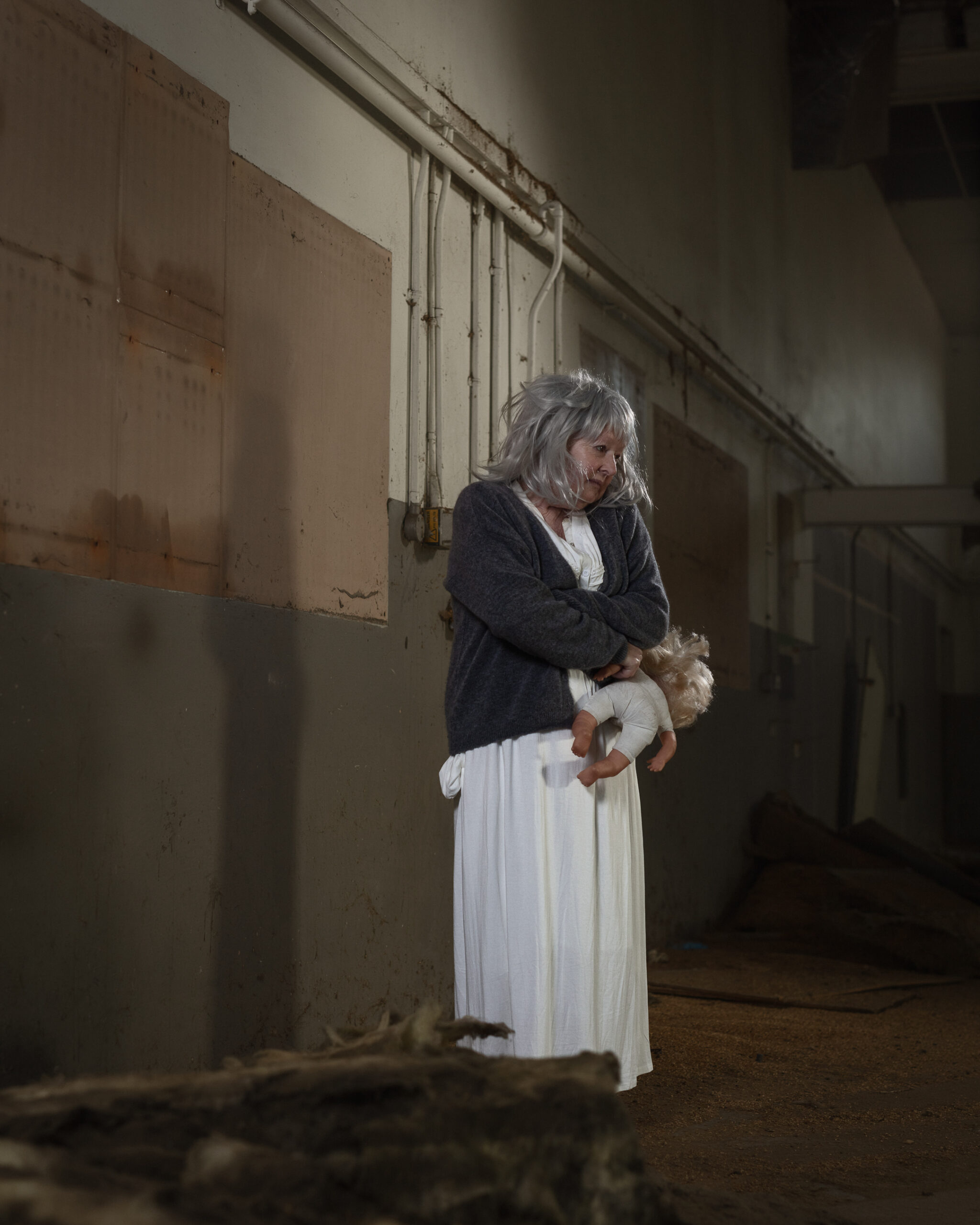 Elderly woman holding doll in abandoned building.