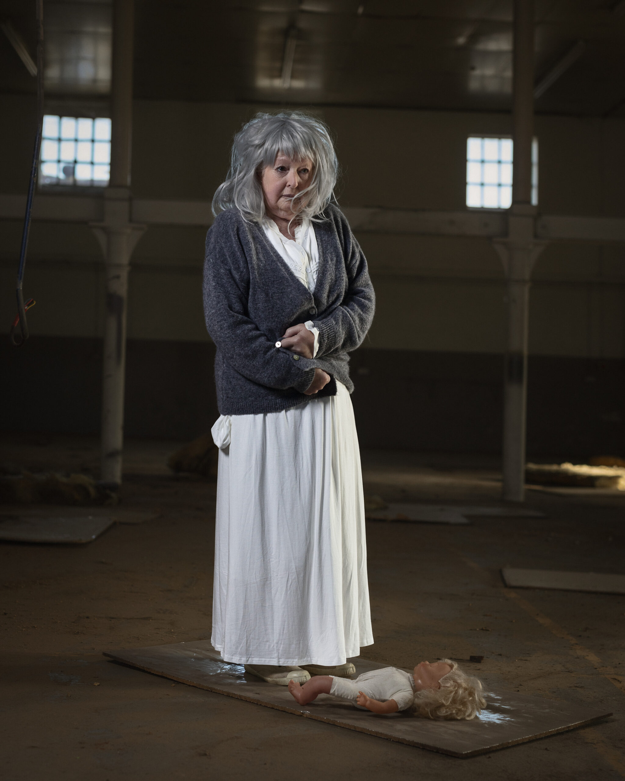 Woman in abandoned building with doll on floor.