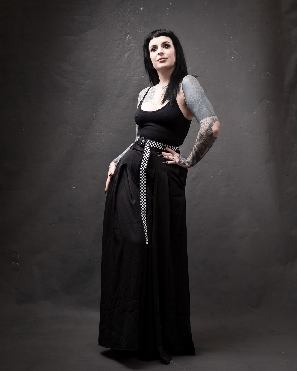 Tattooed woman in black clothing posing elegantly.