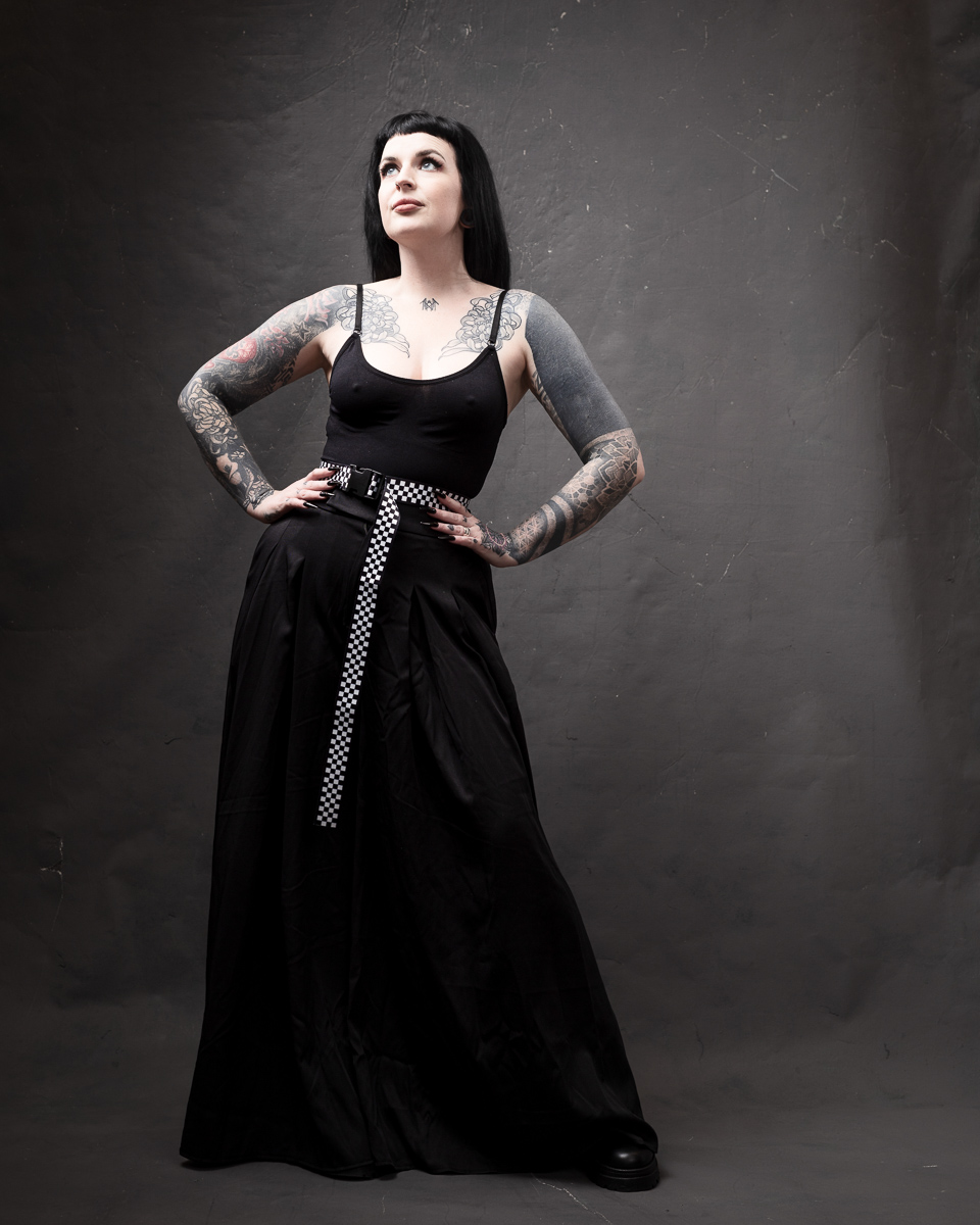 Woman with tattoos in black dress, looking confident.