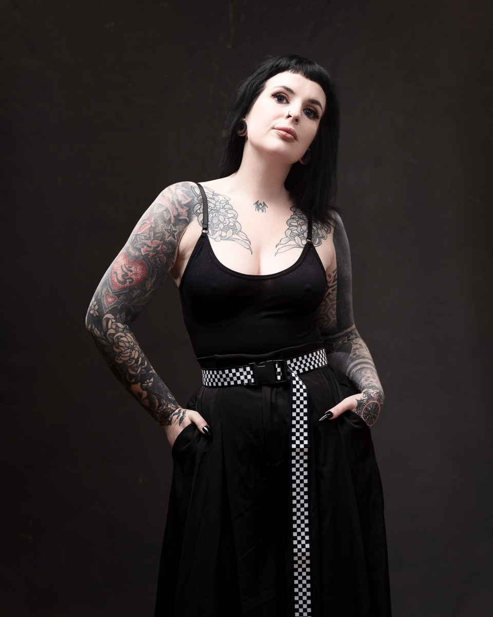 Tattooed person in black outfit, confident pose