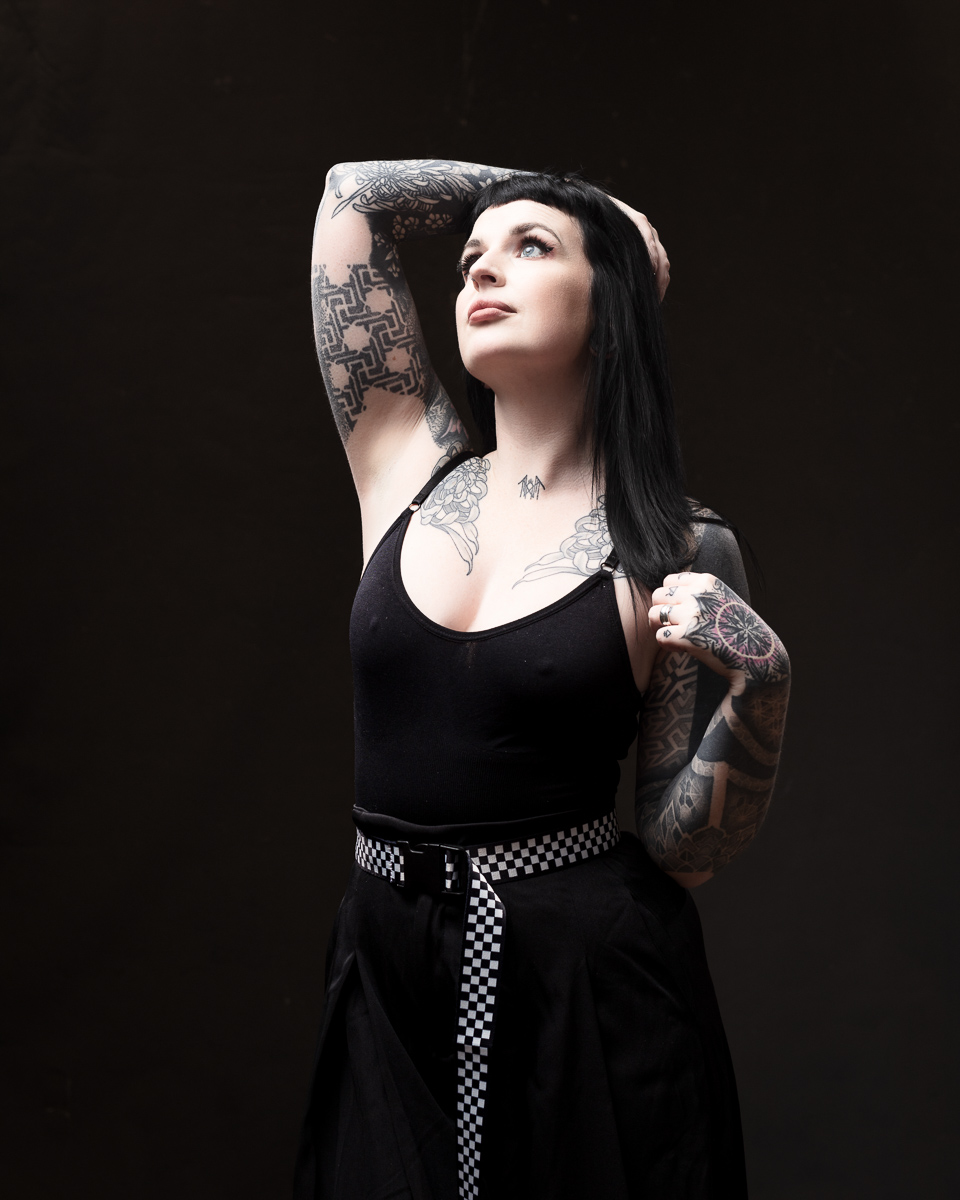 Tattooed woman posing confidently against dark background.