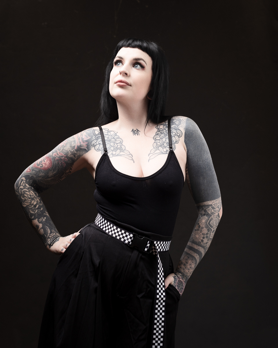 Tattooed woman in black outfit posing confidently.