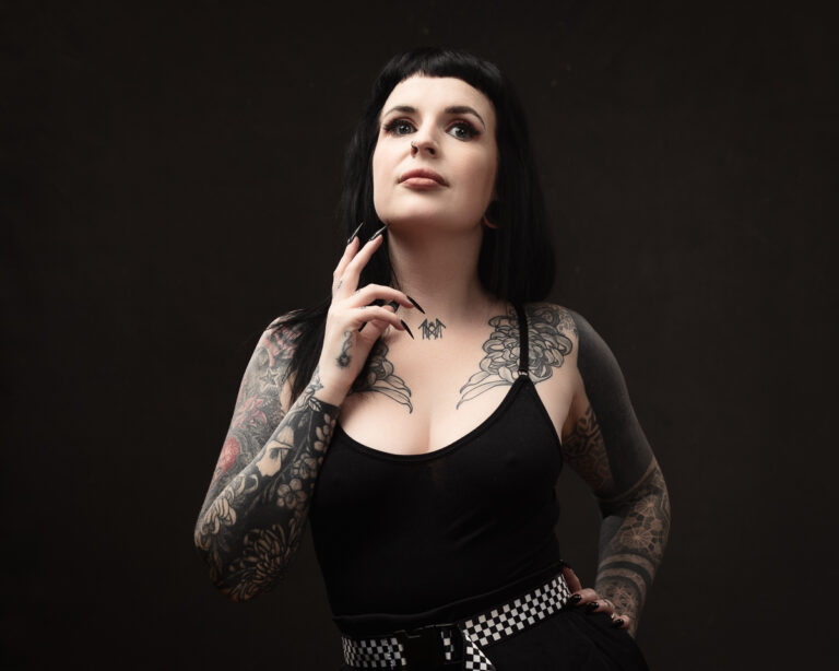 Tattooed woman posing with confidence against dark background.