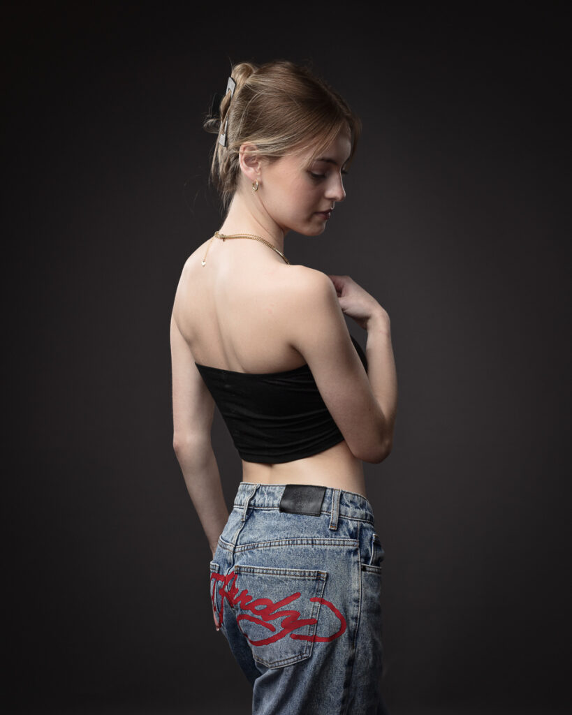 Woman in jeans and black top posing sideways.