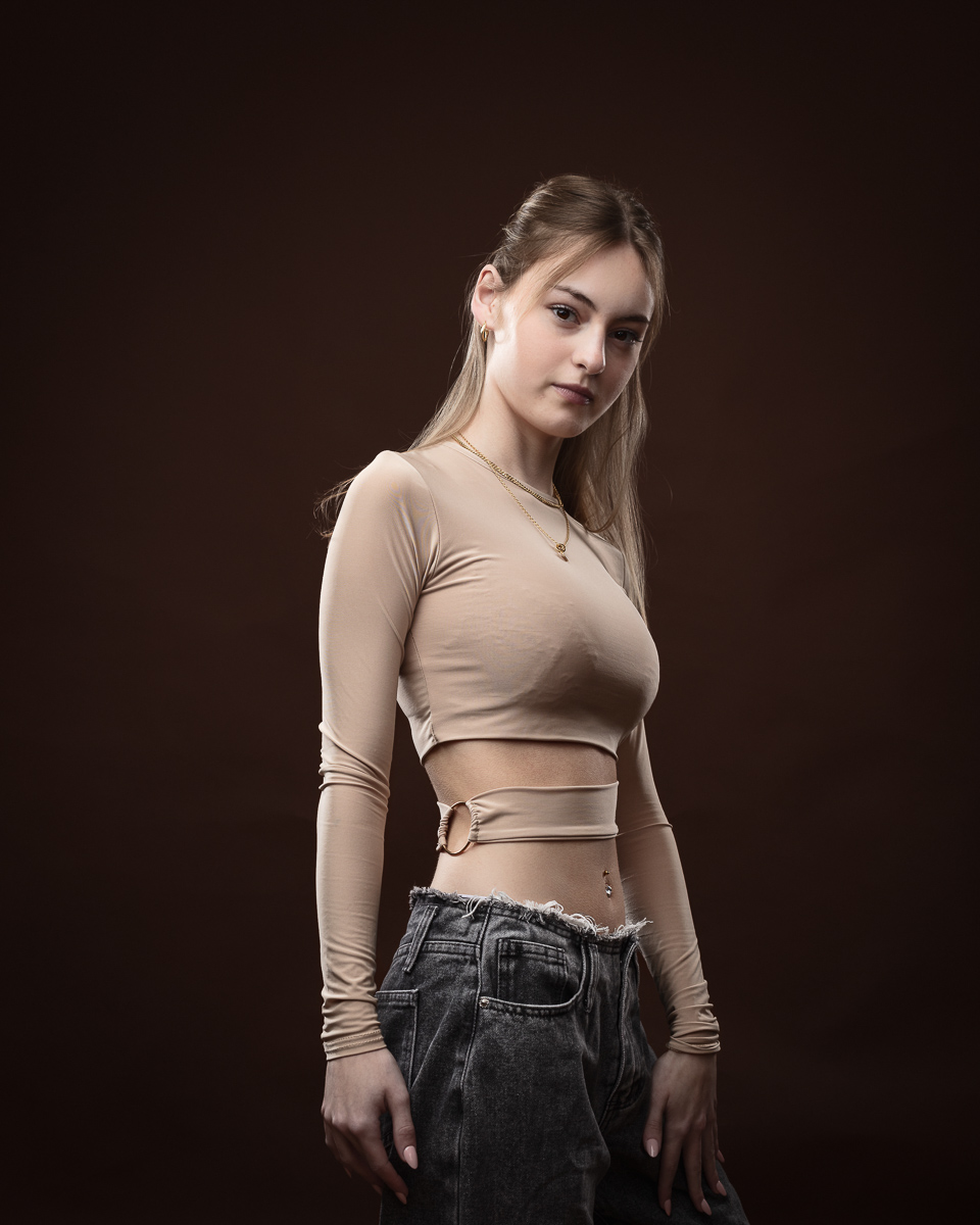 Woman in beige top and jeans, dark background.