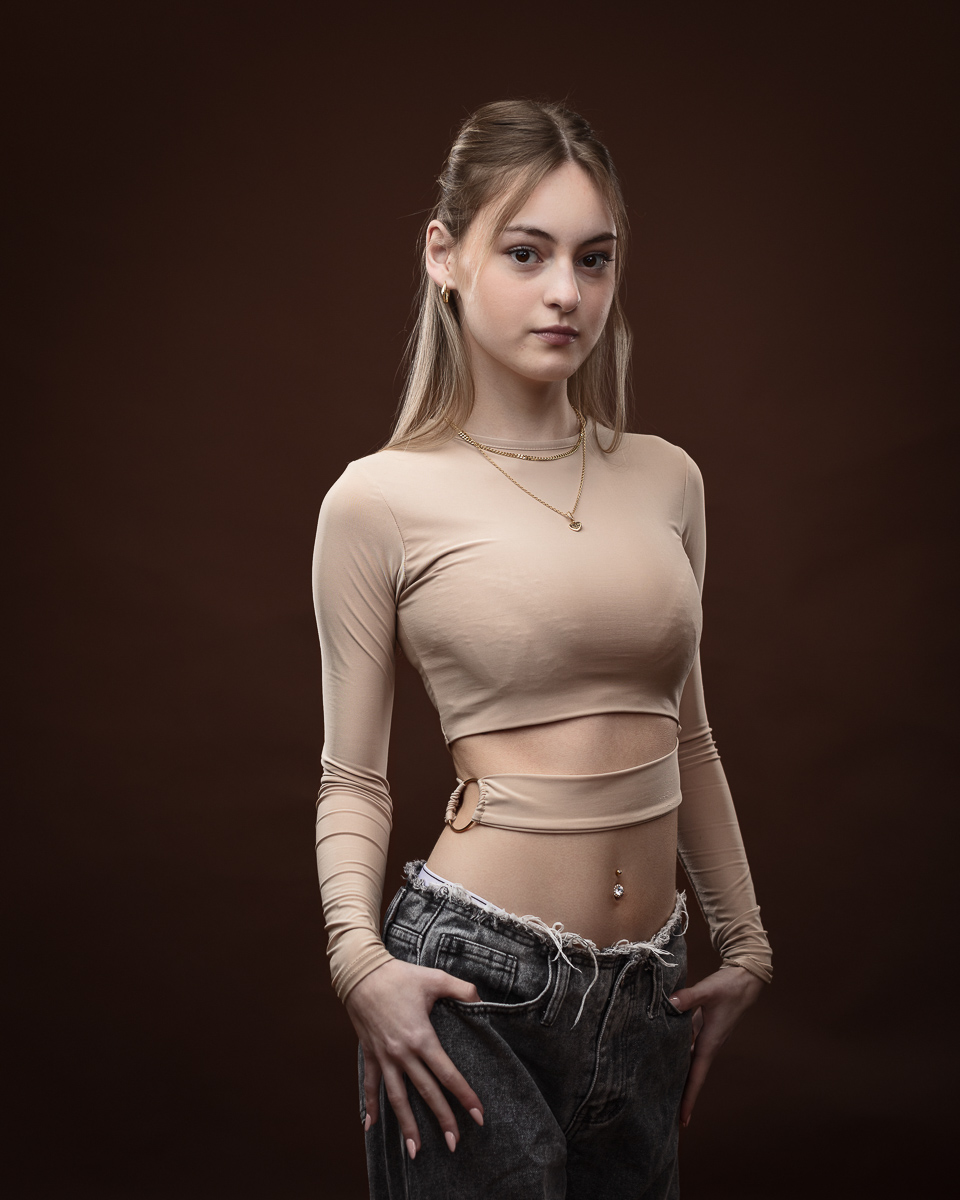 Woman in beige top and jeans on brown background.