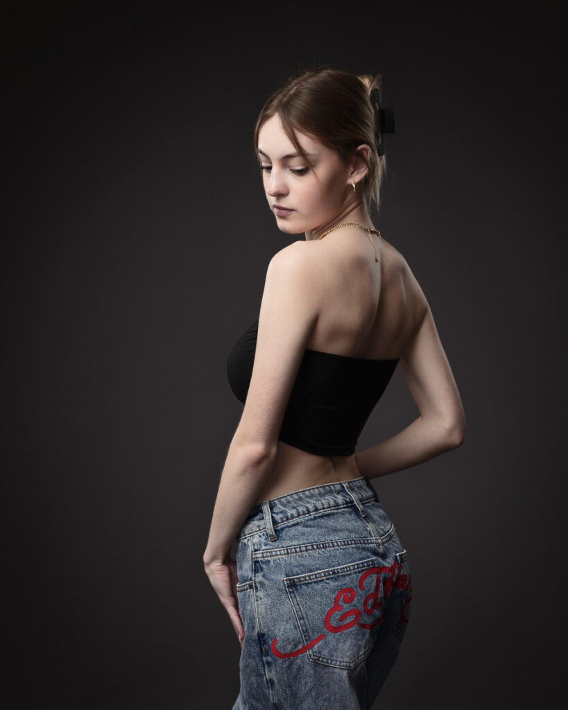 Woman in black top and jeans against dark background.