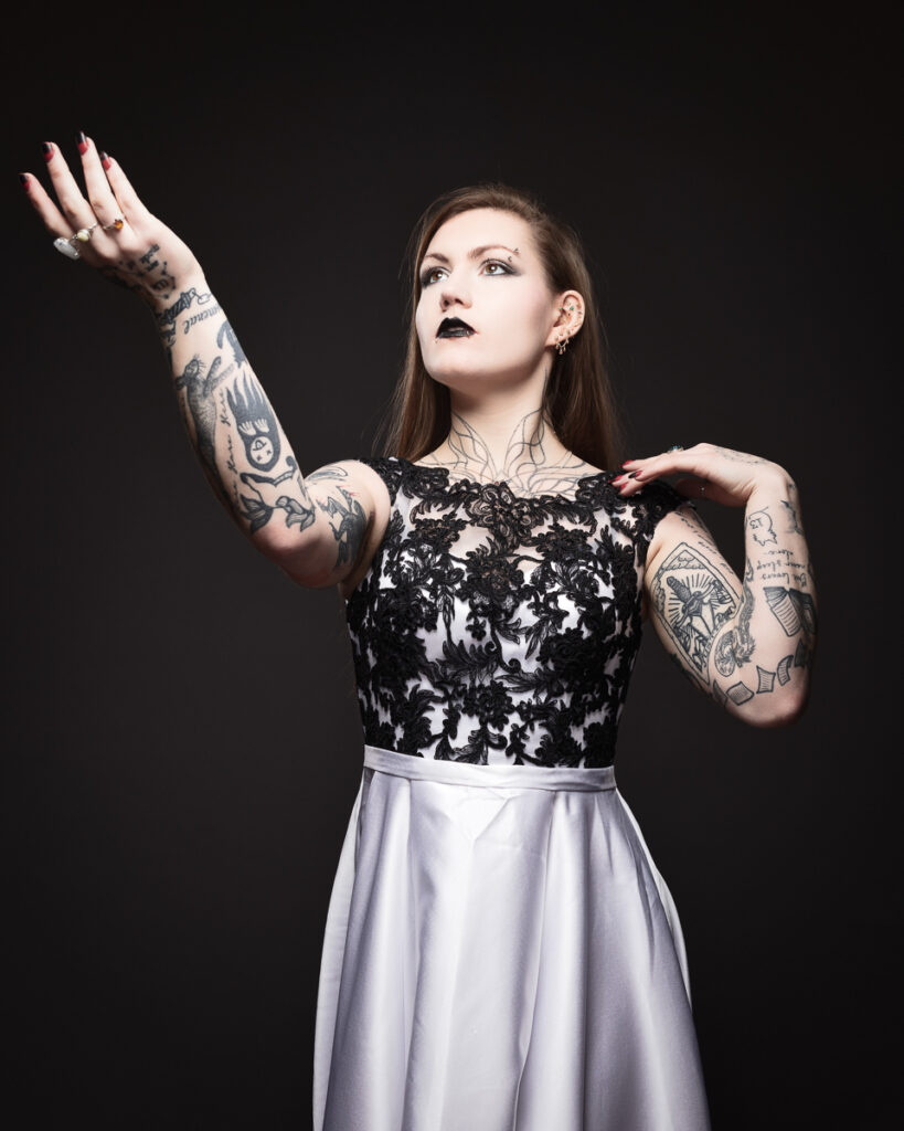 Tattooed woman in elegant dress poses dramatically.