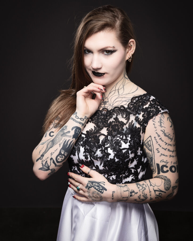 Woman with tattoos wearing a lace dress, posing.