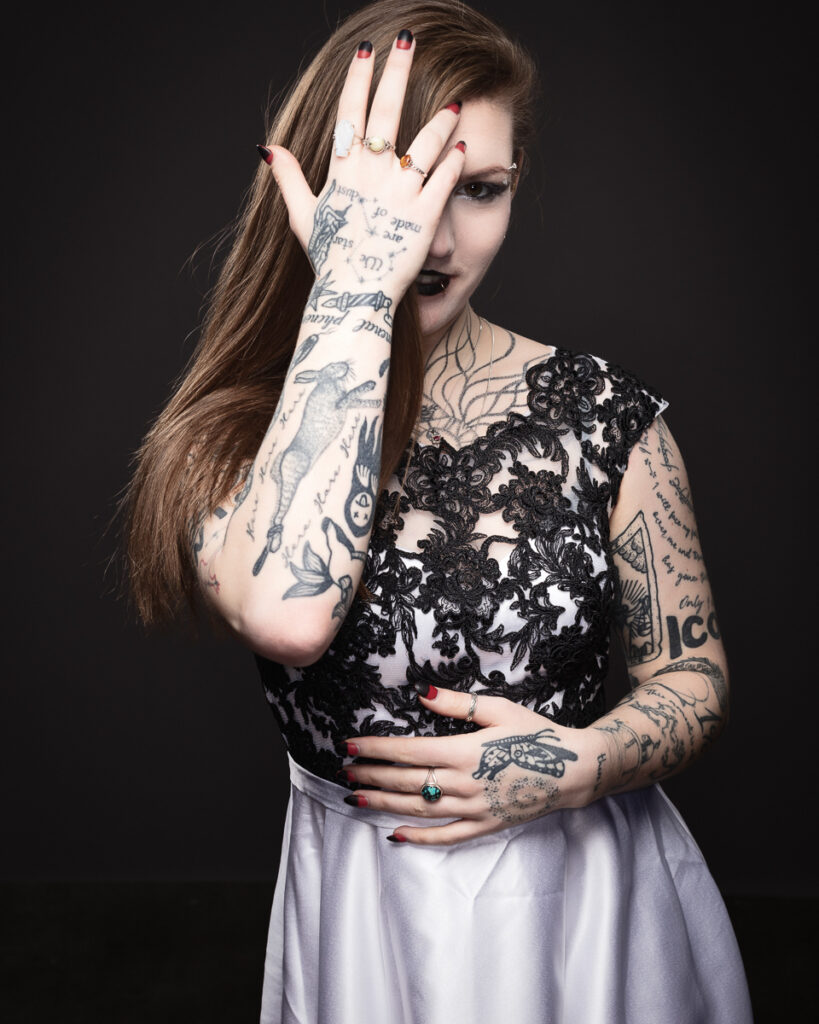 Tattooed woman in lace dress covering face.
