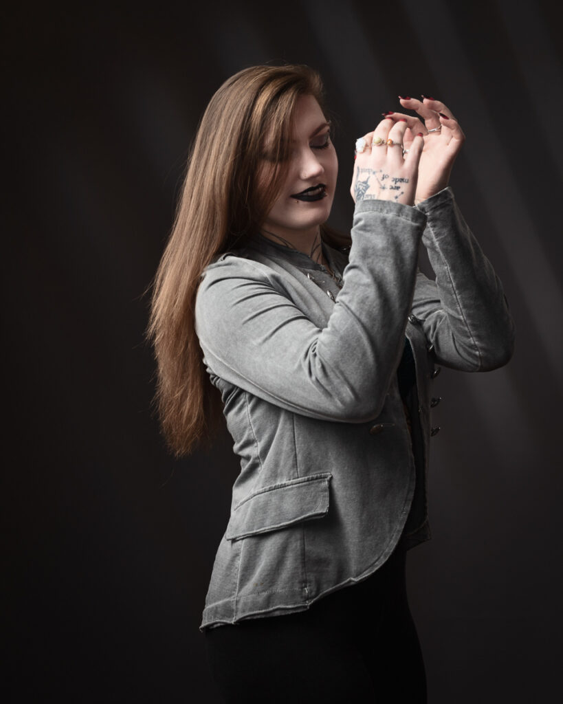 Person with tattoos, wearing grey jacket, dark background.