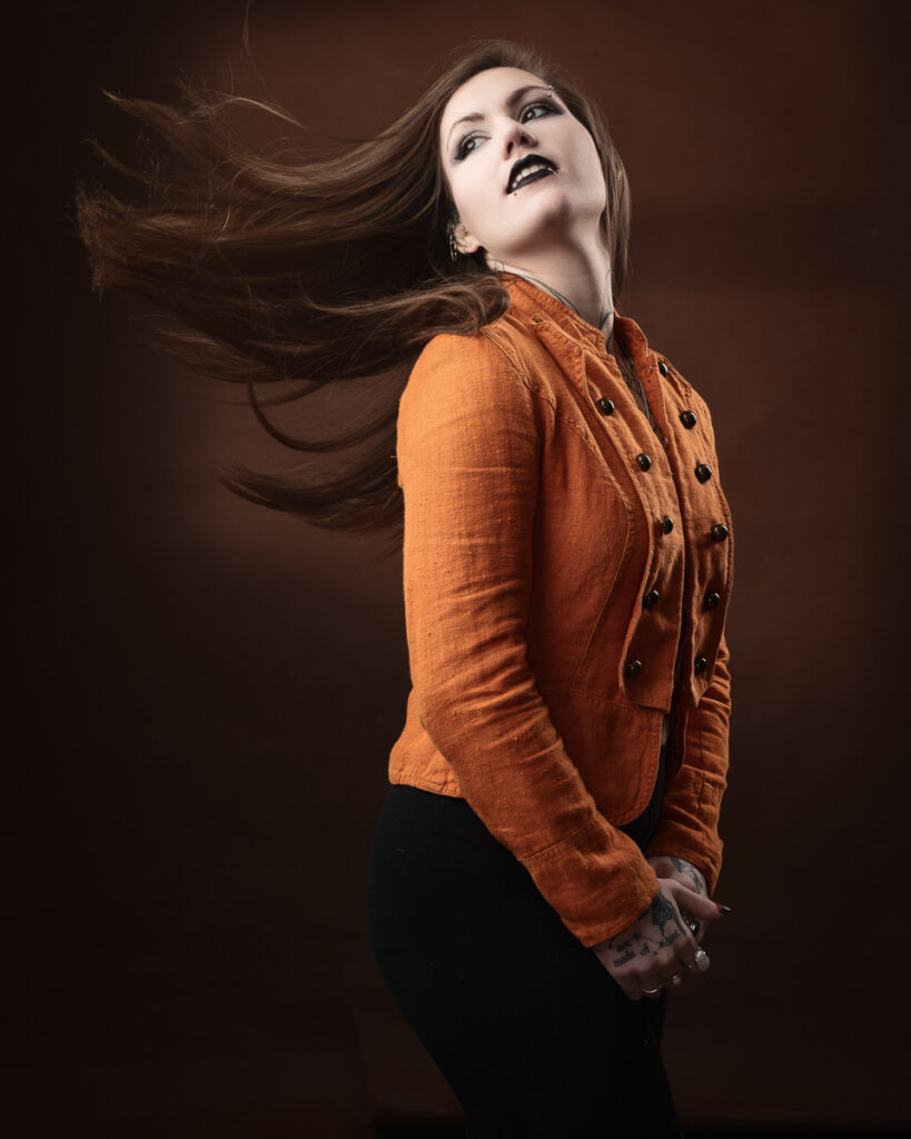 Woman with long hair in orange jacket poses.