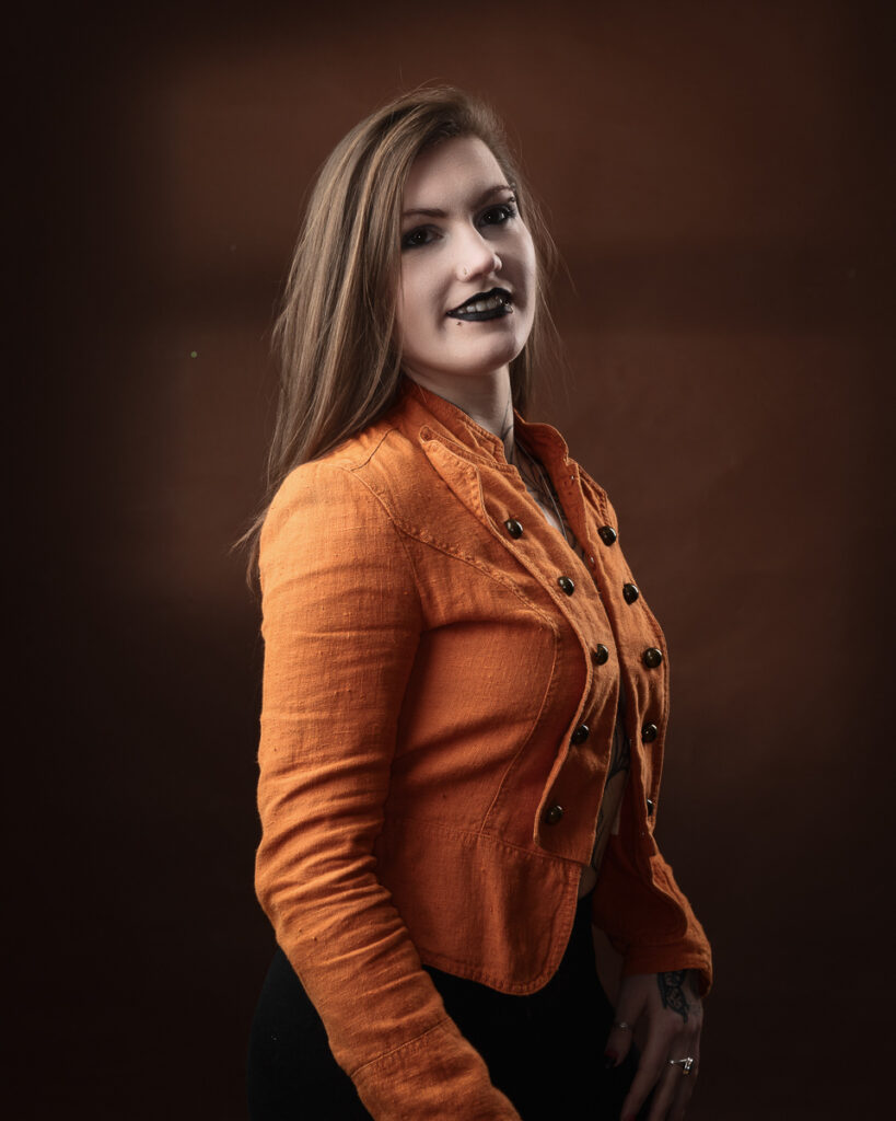 Person in orange jacket with dark lipstick smiling.