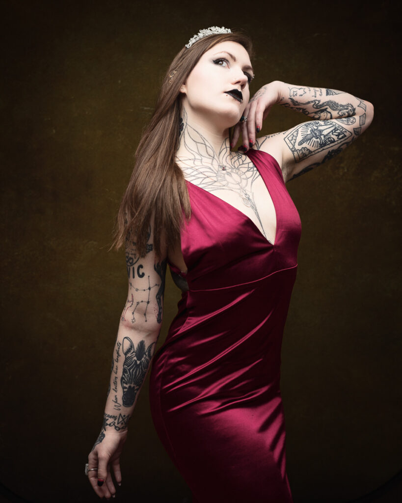Tattooed woman in red dress with tiara posing.