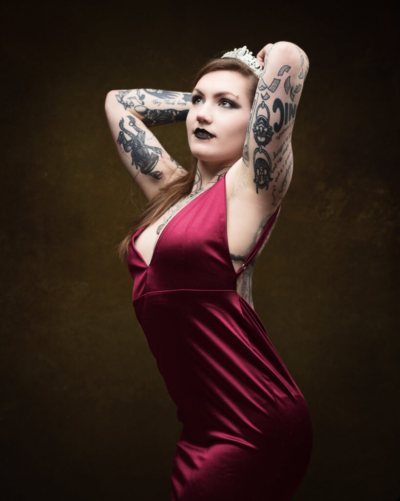 Tattooed woman in red dress and crown poses confidently.