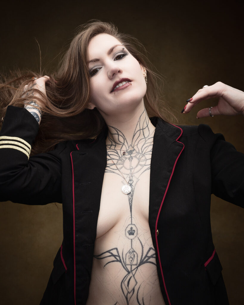 Person with tattoos poses in black jacket.