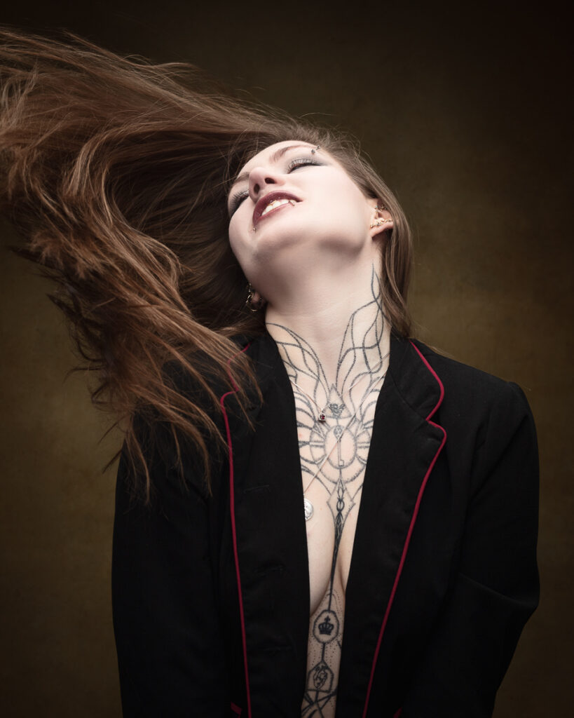 Person with tattoos, hair flowing, wearing black jacket.
