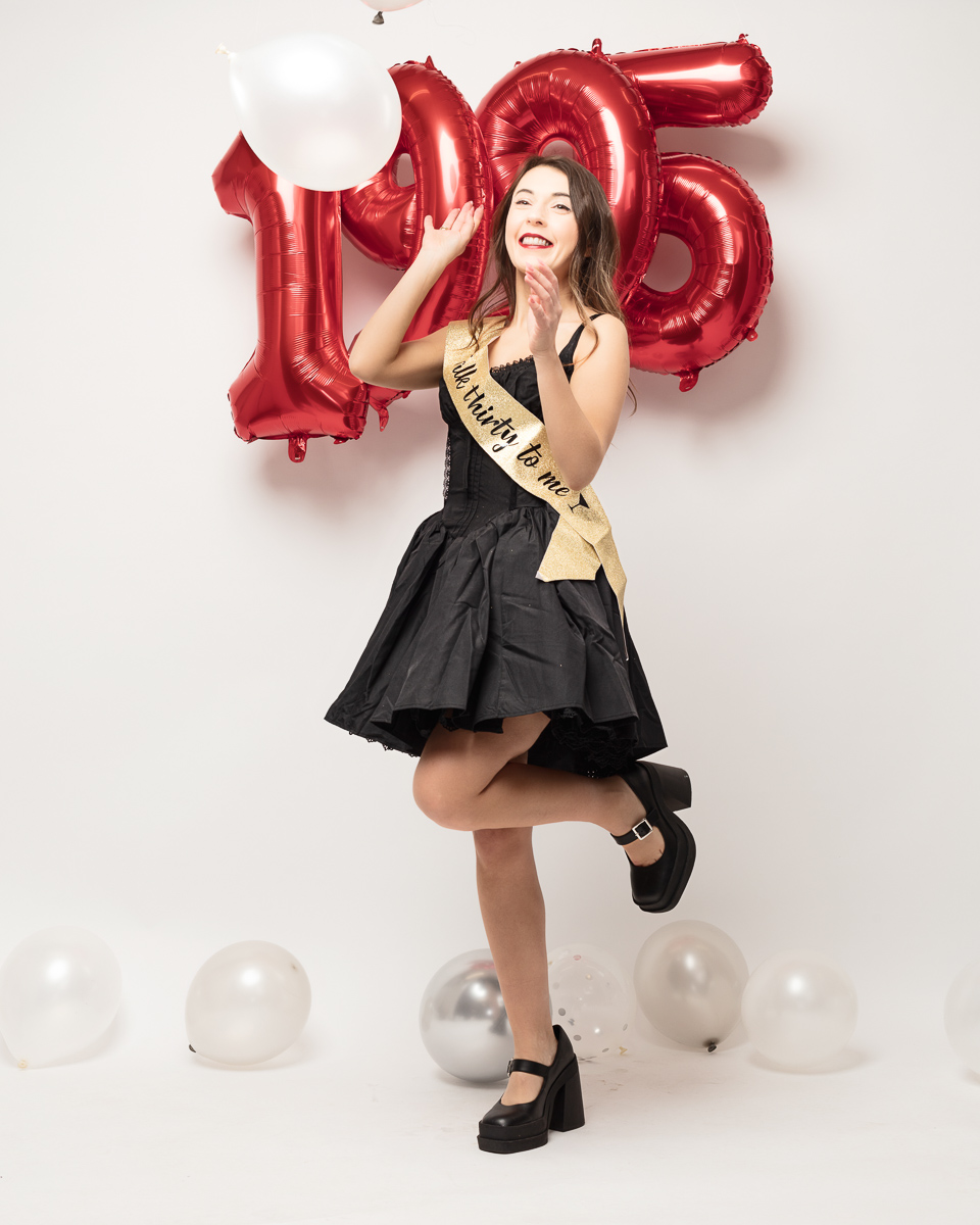 Woman celebrating with 'Happy Birthday' sash and balloons.