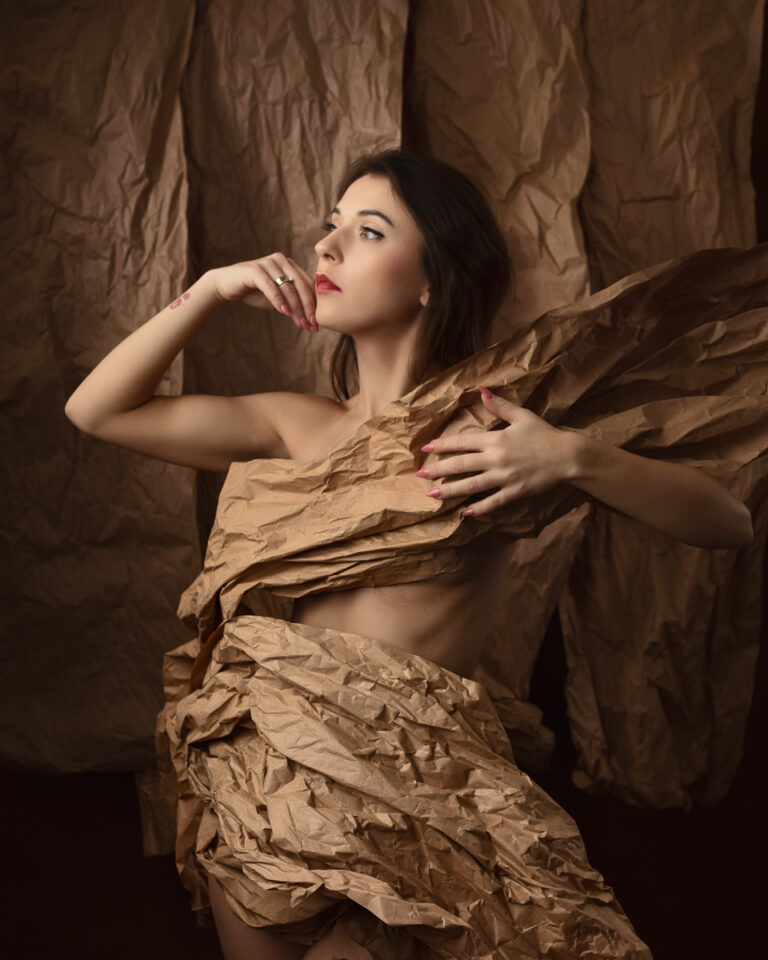 Woman wrapped in crumpled brown paper, artistic pose.