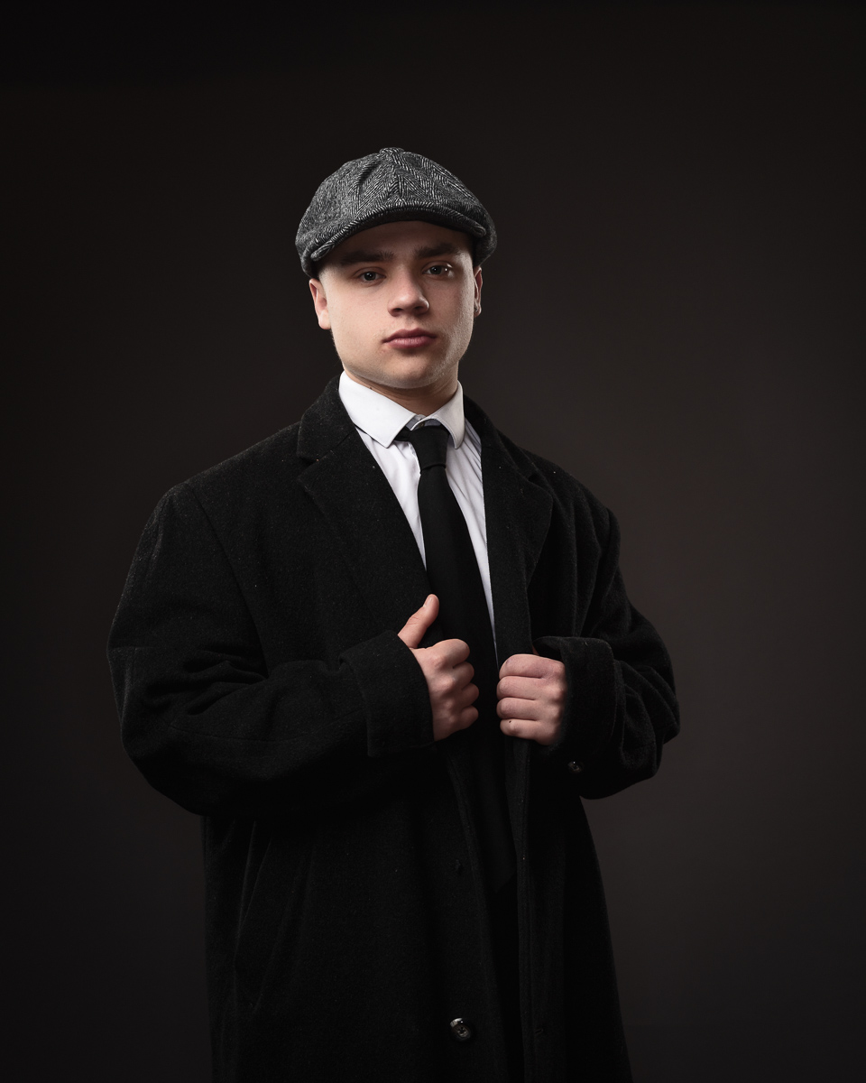 Person in suit and flat cap posing confidently.