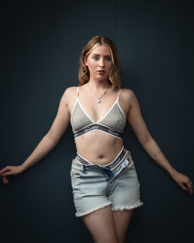 Woman in denim shorts and bralette against dark background.
