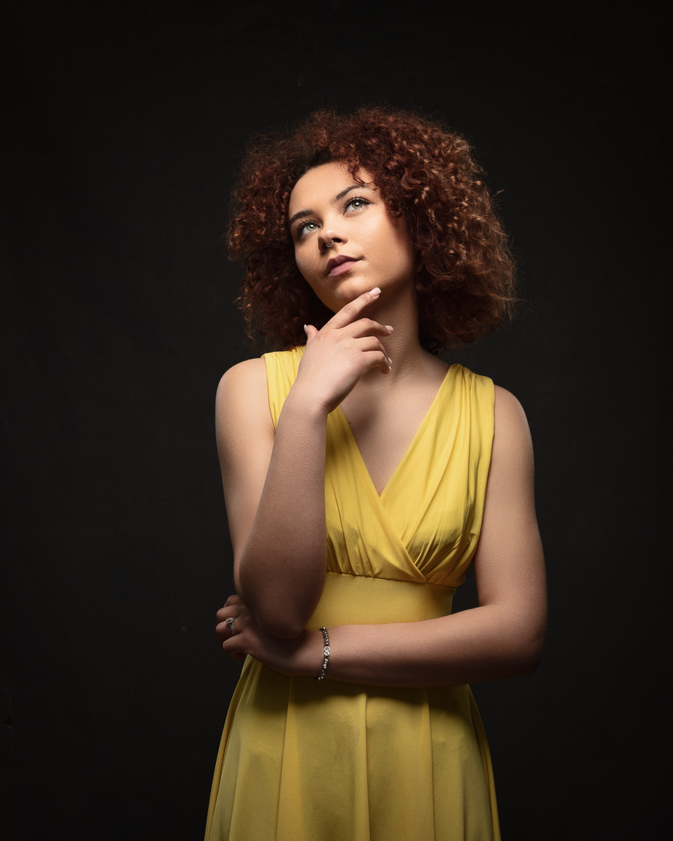 Woman in yellow dress looks thoughtfully upward.