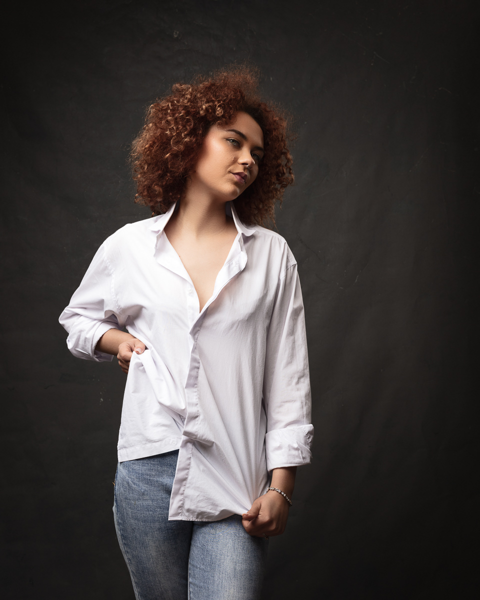 Woman in white shirt posing against dark background.