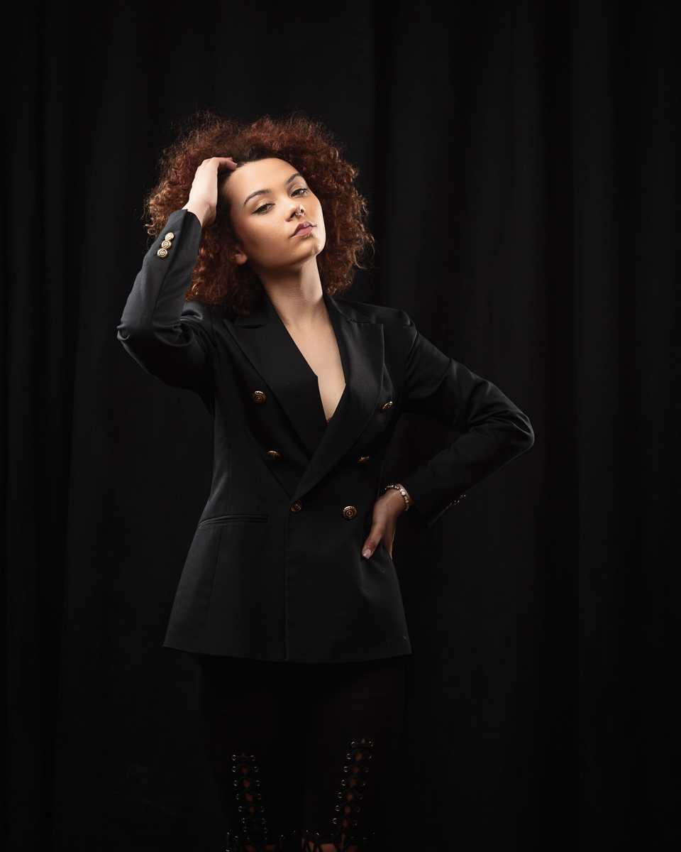 Woman posing in black blazer with curly hair.